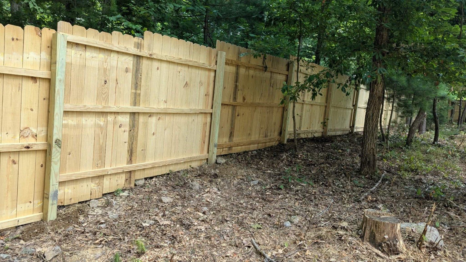 Wood privacy fence installed along wooded terrain